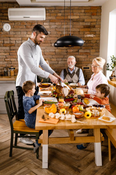 dalsza rodzina jedząca obiad w święto dziękczynienia w jadalni. - roast turkey turkey cutting roasted zdjęcia i obrazy z banku zdjęć