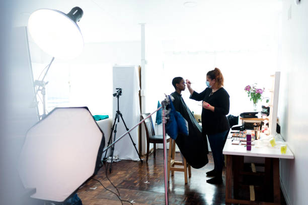 Wide shot backstage make up artist wearing protective face mask working with model