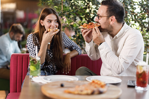 Young couple eating pizza during lunch in a restaurant. Focus is on man.