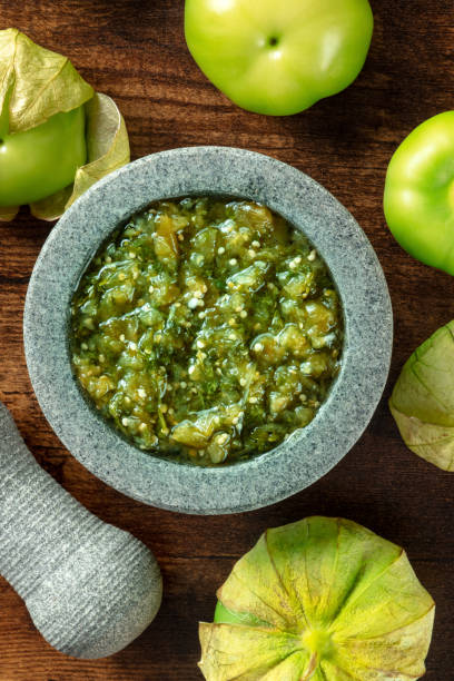 Tomatillos, green tomatoes, with salsa verde, green sauce, in a molcajete Tomatillos, green tomatoes, with salsa verde, green sauce, in a molcajete, traditional Mexican mortar, top shot on a dark rustic wooden background tomatillo photos stock pictures, royalty-free photos & images