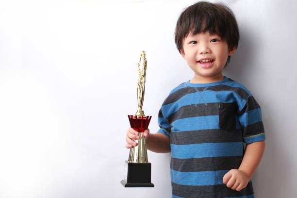 istock Little Asian Boy Holding A Trophy Standing Against White Background 1338610541