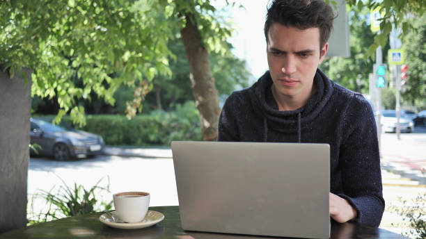 istock Young Man Typing on Laptop while Sitting in Cafe Terrace 1338612124