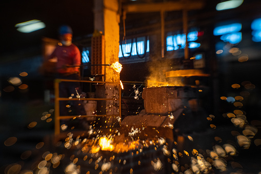 Mature metal worker checking molten metal while working in foundry.