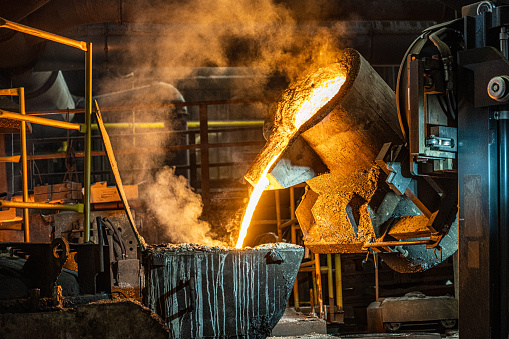 Pouring liquid molten metal from transport vessel to casting mold using forklift in steel mill.