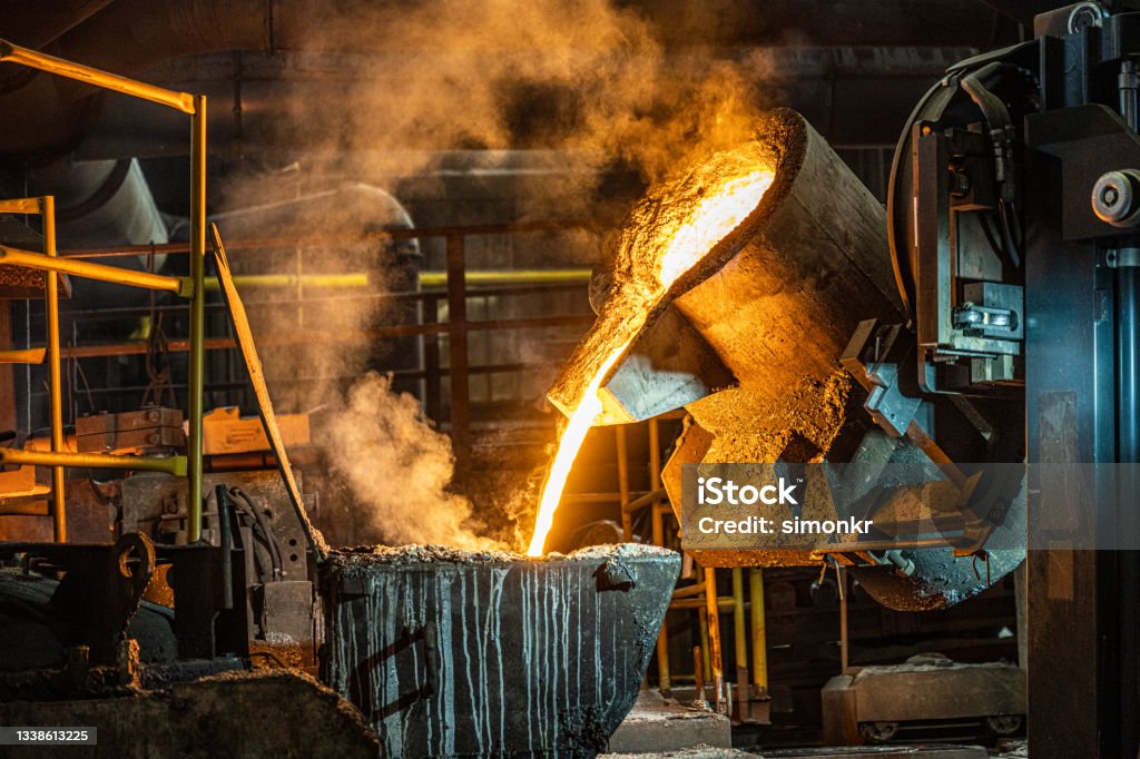 Pouring of liquid molten metal to casting mold using forklift Pouring liquid molten metal from transport vessel to casting mold using forklift in steel mill. Steel Mill Stock Photo