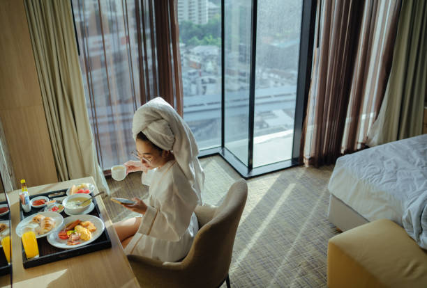 mujer sentada sosteniendo una taza de café y usando el teléfono - bathrobe women cup towel fotografías e imágenes de stock