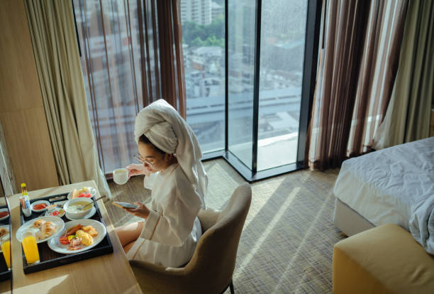 donna seduta con una tazza di caffè e usando il telefono - bathrobe women cup towel foto e immagini stock
