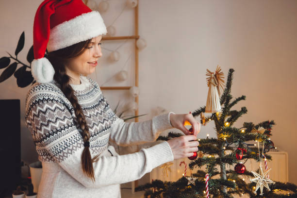 istock Smiling woman wearing Santas hat decorating Christmas tree 1338615995