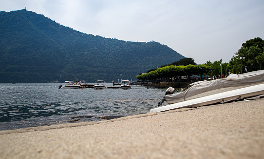 Lakeside view of lake Como, with a couple of small boats, mountains in the background