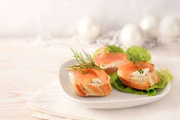 istock Baguette bread canapes with salmon and cream cheese on a white plate with lettuce, light wooden table with festive Christmas decorations, copy space, selected focus 1338623011