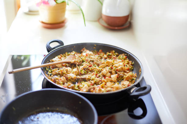 Paella pan with rice chicken and vegetables, wooden spoon, cooking in kitchen home