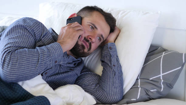 hombre usando un teléfono inteligente mientras está acostado de lado en la cama - 16296 fotografías e imágenes de stock