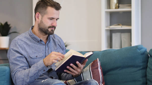 젊은 남자 독서 책, 소파에 앉아 - 16192 뉴스 사진 이미지