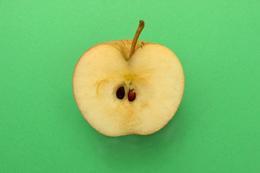 Stock photo showing elevated view of a green, stalked apple cut in half displaying seeds, against a green background.