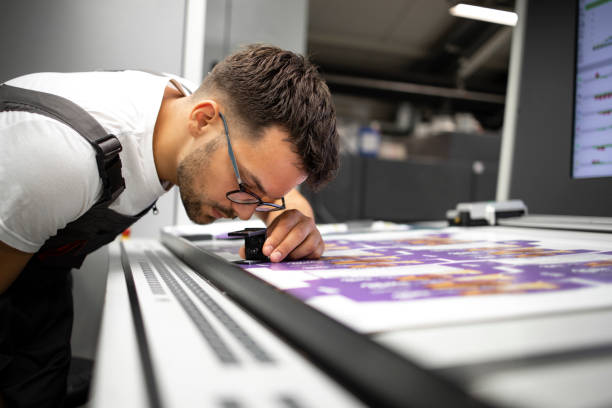 Worker checking print quality of graphics in modern printing house. Worker checking print quality of graphics in modern printing house. printing plate photos stock pictures, royalty-free photos & images