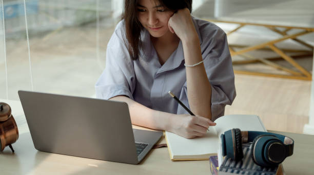 istock Online education. Asian girl taking note for online lesson using a computer video call to a virtual teacher at home 1338632736