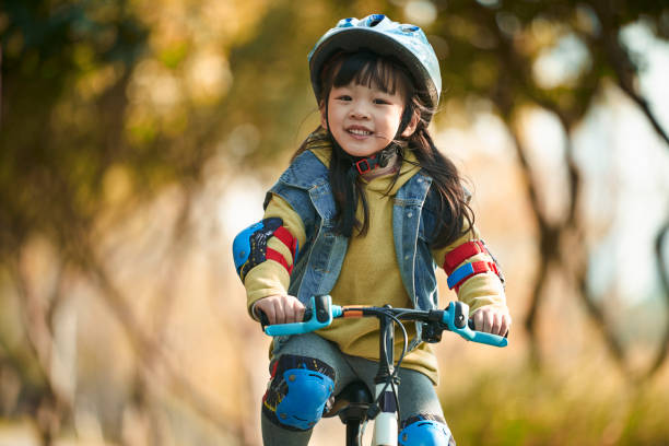 happy little asian girl riding bike in park - helmet bicycle little girls child imagens e fotografias de stock
