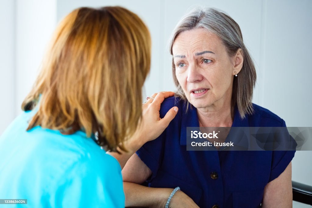 Depressed senior woman talking with nurse Worried elderly woman talking with nurse. Close up of face. Parkinson's Disease Stock Photo
