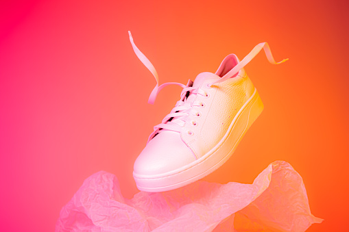 Fashion - white leather sneakers shoe. Footwear levitating on the bright pink and orange background. Layout with free copy (text) space.