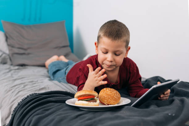 boy at home young boy eating unhealthy food and using digital tablet while sitting in his room terrible meal stock pictures, royalty-free photos & images