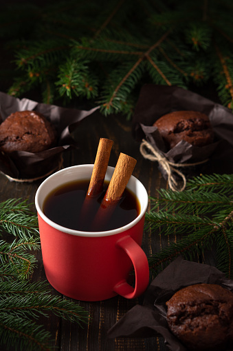Pink ceramic mug with black tea and cinnamon on a dark wooden background, delicious chocolate muffins for tea among fir branches, Merry Christmas and Happy New Year