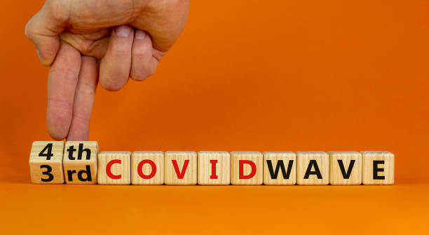 istock Symbol for a 4th wave of the covid-19 corona virus. Doctors turns cubes, changes words 3rd covid wave to 4th covid wave. Beautiful orange background. Fourth wave of the covid-19 concept. Copy space. 1338649215