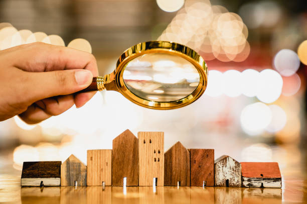 Hand holding magnifying glass and looking at house model, house selection, real estate concept. stock photo