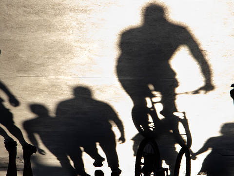 Blurry shadow silhouette of people walking and riding bikes on a promenade on a summer day, in sepia black and white