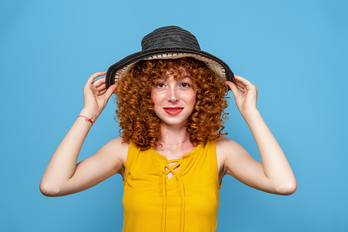 Red and curly hair beautiful woman with a hat isolated on blue background. High quality photo