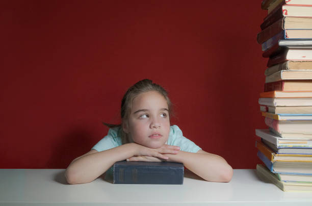 garota com livros em uma mesa branca em um fundo vermelho. de volta à escola. emoção - confusão - child prodigy - fotografias e filmes do acervo