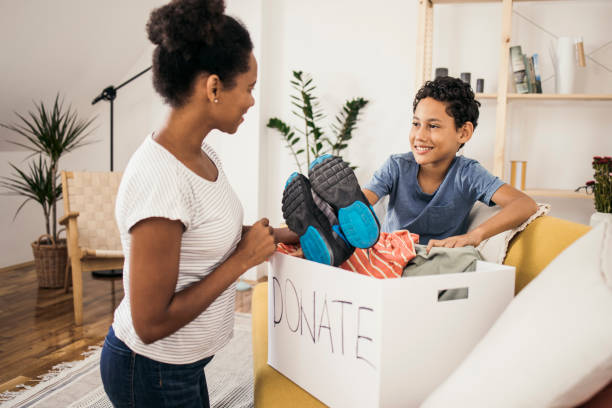 Mother and son preparing a box of clothes for donation African American woman and her son packing old clothes into the donation box. clothing donation stock pictures, royalty-free photos & images