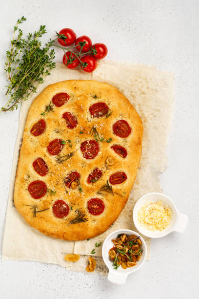 italienisches traditionelles focaccia-brotbacken mit kirschtomaten, parmesan und rosmarin auf hellbraunem hintergrund. draufsicht - italian cuisine gluten free food tomato herb stock-fotos und bilder