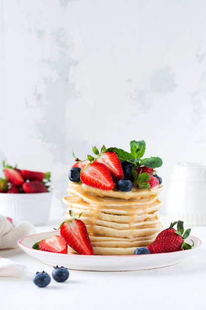 istock Breakfast pancakes. Stack of pancakes with fresh blueberries and strawberries on plate with bowls of strawberries and blueberries on light slate, stone or concrete background. Top view. copy space 1338655992