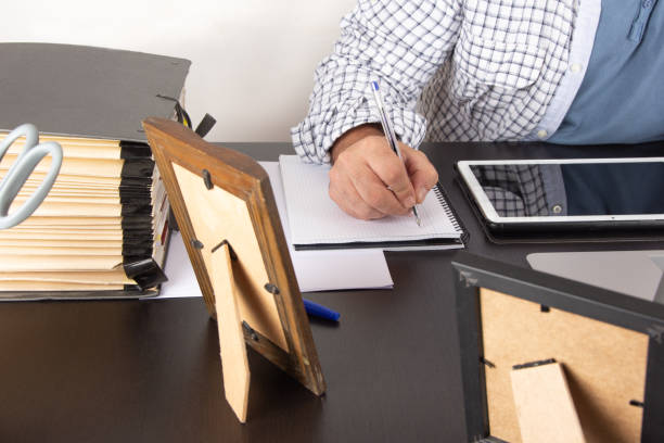istock arm of a businessman taking notes in a notebook on his home desk with tablet and computer and a filing cabinet folder 1338657862