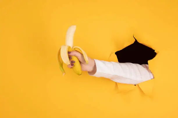 Female hand Holding Banana Fruit, Nutrition concept, human hand holding a banana in hole orange background