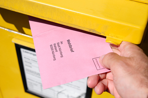 Nuremberg, Germany - September 09, 2021: A male hand inserting a Wahlbrief ( election letter ) into the mail slot of a yellow letter box for the Bundestagswahl 2021 ( federal elections ) in Germany