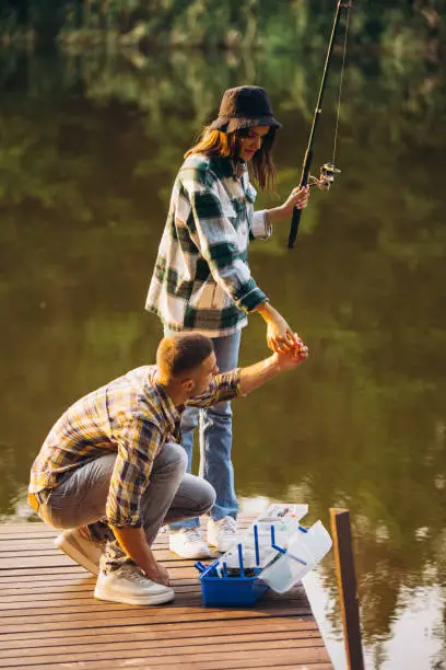 Young beautiful couple fishing on river together on warm summer day. Putting fish bait on hook. Having fun, breathing fresh air. Extraordinary romantic day. Concept of relationship, leisute time, ad