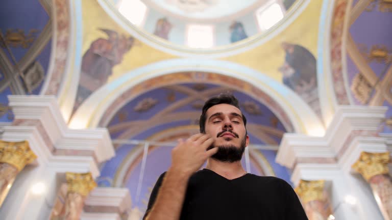 Young man praying in church, Young man crosses in church, People attending religious mass in cathedral