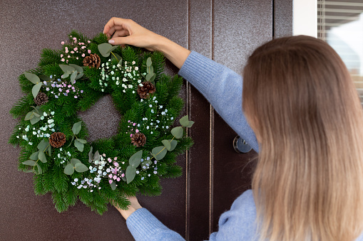 woman hanging Christmas wreath on front door. house decorating for Christmas holiday