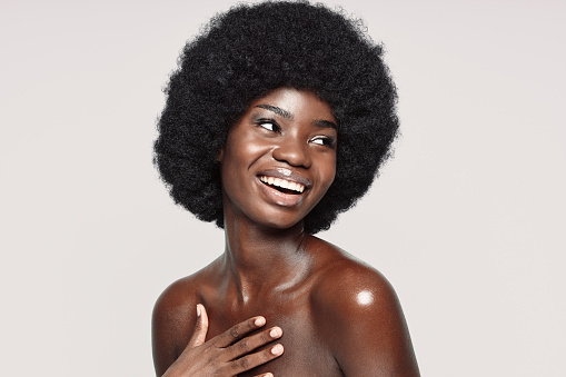 Portrait of beautiful young African woman looking away and smiling while standing against gray background