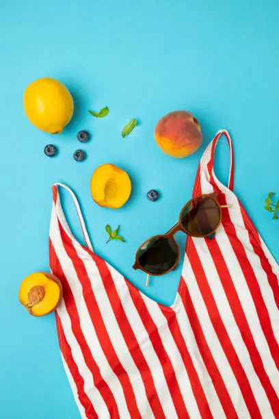 Photo of Female striped bright red swimsuit, peaches, lemons, sunglasses on a bright blue background. Travel concept. Flat lay, top view.