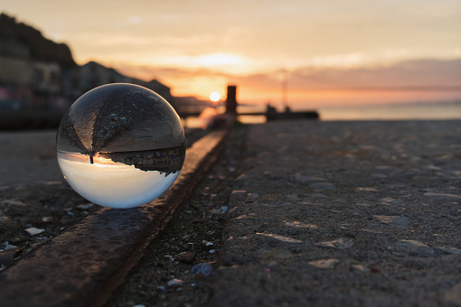 A close up image of a hand holding a photography glass lens ball against a golden sunset along the ocean shoreline.