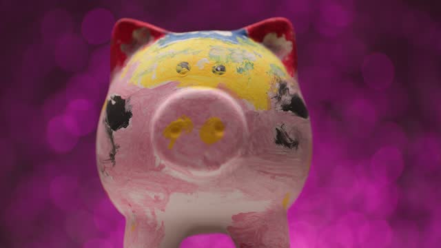 project video showing and presenting colorful painted piggy bank in front of pink lights background moving right and left