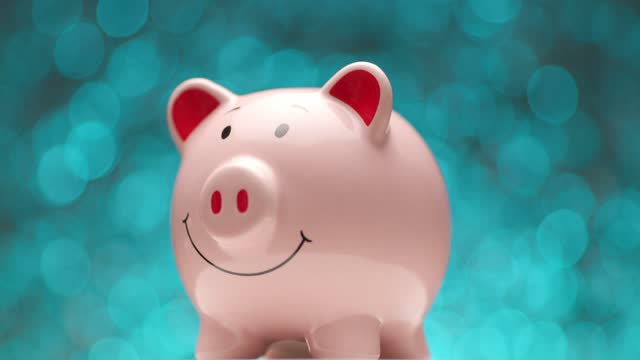 project video presenting pink piggy bank slowly moving left in front of blue lights background in studio