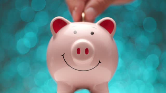 pink piggy bank turning from side view, hands putting coin inside in front of blue lights background