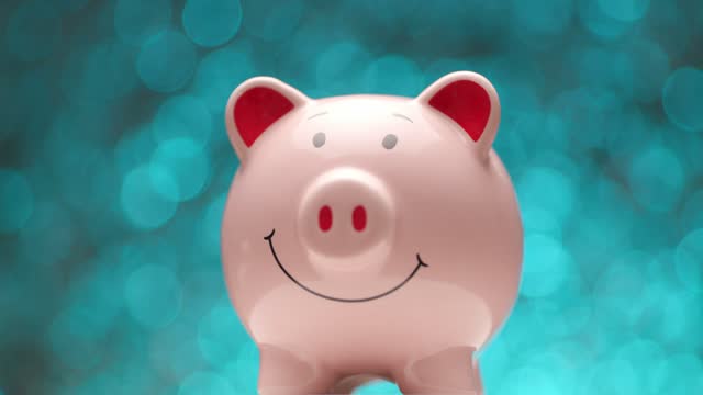 side view of pink piggy bank in front of blue lights background moving and spinning to right