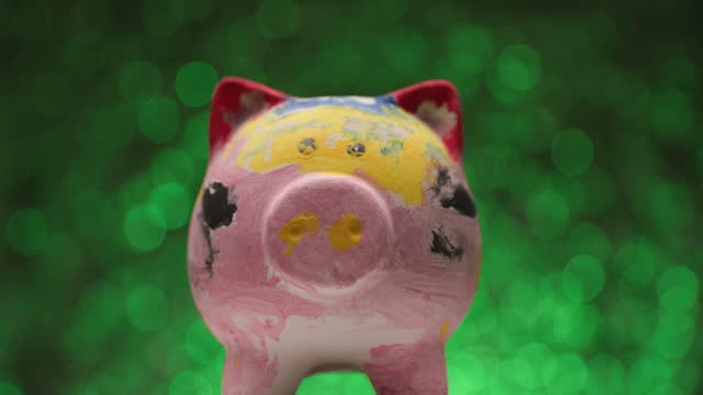 project video of colorful painted piggy bank moving left and right while making a presentation in front of green background