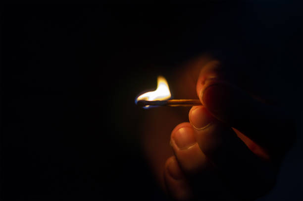 A man's hand with a burning match against a black background. Close-up of a man's hand with a match lit in the night. Defocus, noise, blurred, grain effect.