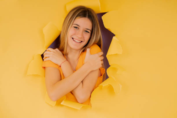 istock Woman embracing herself while standing through a hole on the paper wall. 1338687310