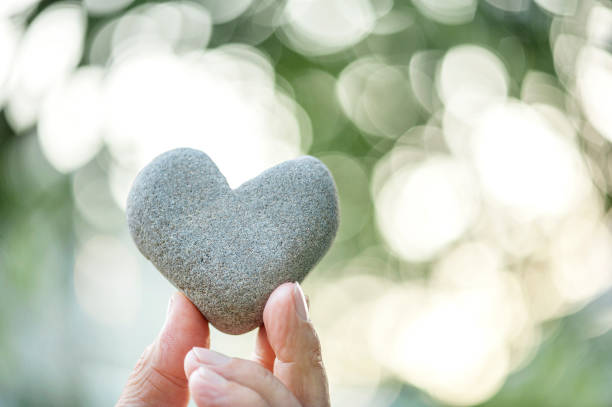 hand holding a heart shaped stone on bokeh background